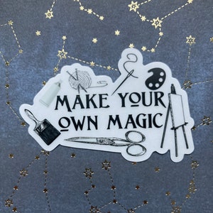 May include: White sticker with black line drawings of art supplies, including paintbrushes, yarn, scissors, and an easel. The text "Make your own magic" is printed in black.