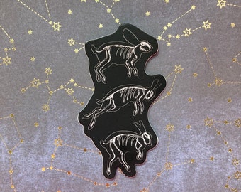 May include: Three black and white skeletal rabbit stickers on a dark gray background with gold stars and constellations.