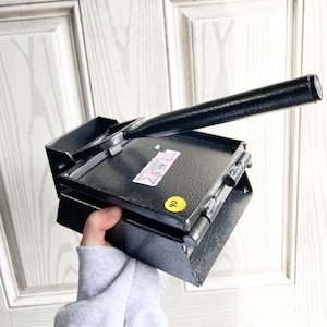 May include: A black metal tool with a long handle and a hinged platform. A sticker with a pink and white design is on the platform, along with a yellow sticker with the number 40.