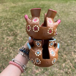 May include: Two brown ceramic pots stacked on top of each other. Each pot has a unique shape with a handle and is decorated with white and pink floral patterns. The pots have blue and pink accents.