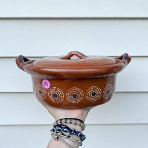 May include: A brown ceramic cooking pot with a lid. The pot has a circular design with white dots and blue centers. The pot has two handles and a handle on the lid. A pink price tag with the number 20 is on the side.