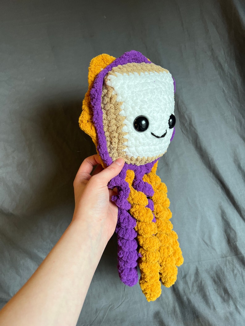 May include: A crocheted plush toy shaped like a smiling octopus with a white head, brown and white body, and purple and yellow tentacles.