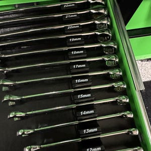 May include: A set of chrome combination wrenches neatly organized in a black tray within a green toolbox drawer. Each wrench is labeled with its size in millimeters, ranging from 11mm to 22mm.