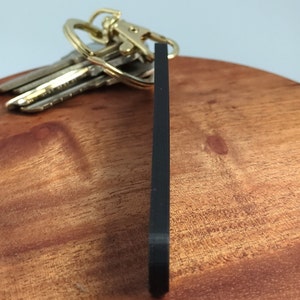 May include: A black keychain with a gold key ring. The keychain is made of a thick, durable material and is designed to be long-lasting.