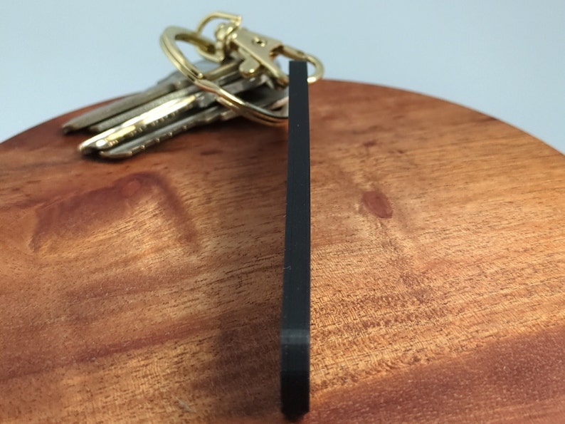 May include: A black keychain with a gold key ring. The keychain is made of a thick, durable material and is designed to be long-lasting.