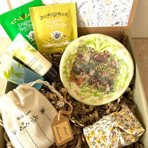 Può includere: Una confezione regalo contenente bustine di tè, lozione per il corpo, un piatto decorativo con una scena di giardino, una piccola borsa con la scritta "With love" e un articolo confezionato. Il piatto presenta la scritta "The Secret Garden".