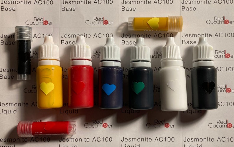 K&ouml;nnte beinhalten: Ein Satz von acht Harz-Pigmentflaschen in verschiedenen Farben, darunter Gelb, Rot, Blau, Gr&uuml;n, Wei&szlig; und Schwarz. Die Flaschen sind mit "Jesmonite AC100 Liquid" beschriftet.