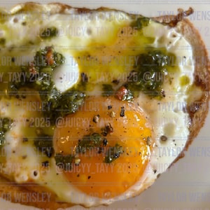 Könnte beinhalten: Nahaufnahme eines Spiegeleis auf Toast mit Pesto, roten Pfefferflocken und schwarzem Pfeffer. Der Toast ist goldbraun und das Eigelb ist flüssig.