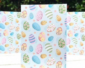 May include: Three blank greeting cards with a light blue background and a pattern of colorful Easter eggs. The eggs are decorated with stripes, dots, and flowers.