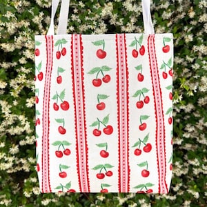 May include: A white tote bag with red and pink stripes and a repeating pattern of red cherries.