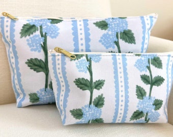May include: Two zippered pouches with a blue and white floral pattern. The pouches are made of canvas and have a gold zipper.