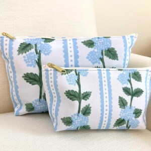 May include: Two zippered pouches with a blue and white floral pattern. The pouches are made of canvas and have a gold zipper.