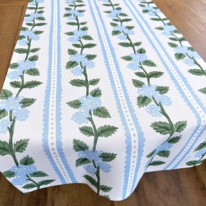 May include: A white table runner with a blue and white striped pattern and a floral design. The flowers are blue and green and are arranged in a vertical line.