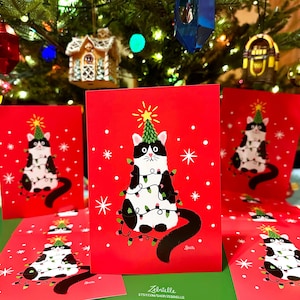 May include: Set of five red Christmas cards featuring a black and white cat wearing a Christmas tree hat and tangled in Christmas lights. The cards have a white snowflake pattern and the text "Zelntalle Etsy.com/shop/Zelntalle"