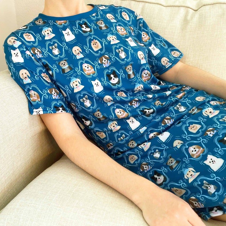 May include: A teal blue short-sleeved t-shirt with a pattern of various dog breeds in different poses. The dogs are all wearing collars and have different colored fur.
