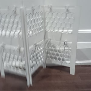 Puede incluir: Divisor de habitación plegable blanco con un patrón de panal. El divisor está hecho de metal y tiene un acabado blanco.