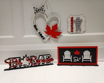 May include: A set of four wooden Canadian themed signs. The signs feature a red maple leaf, a heart with the text "Est. 1967", a sign with the text "Canada" and an Inukshuk, and a sign with two white Adirondack chairs, a red maple leaf, and the text "Eh?"