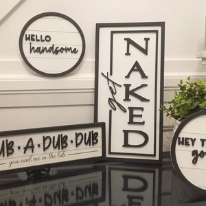 Puede incluir: Cuatro letreros de madera en blanco y negro con diferentes frases sobre el tema del baño. Los letreros dicen "Hello handsome", "Scrub-A-Dub-Dub you and me in the tub", "Get Naked", y "Hey There Gorgeous".