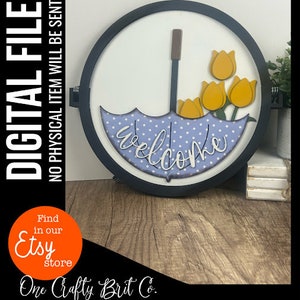 May include: A round wooden sign with a blue and white polka dot umbrella and yellow tulips. The sign says "Welcome".
