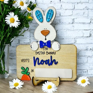 Puede incluir: Señal de madera de conejo de Pascua con ojos azules y una pajarita azul. El letrero dice "El conejito de Pascua visita a Noah en".