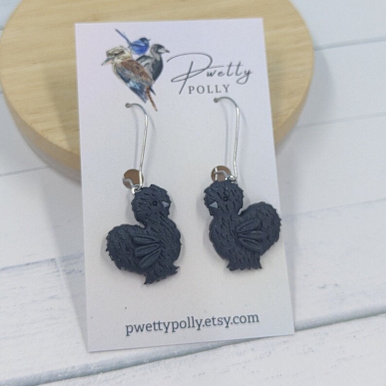 May include: A pair of dangle earrings featuring black silhouetted chickens. The earrings are on a white card with the text "Pwetty Polly" and "pwettypolly.etsy.com".