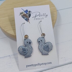 May include: A pair of silver dangle earrings featuring a gray silkie chicken charm with a brown bead accent. The earrings are displayed on a white card with the text "pwettypolly.etsy.com".