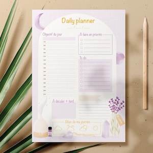Pode incluir: Um planejador diário roxo e branco com um design de lua e estrelas. O planejador tem seções para objetivos diários, lista de tarefas e uma seção para coisas a fazer mais tarde. O planejador também tem uma seção para uma reflexão diária.