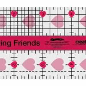 Puede incluir: Una regla de acolchado de plástico transparente con una franja roja en el medio. La franja roja tiene el texto "I ♥ my Quilting Friends" y "creative grids". La regla tiene un patrón de cuadrícula con formas de corazón.
