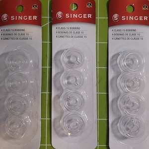 May include: Three packages of Singer brand bobbins for sewing machines. Each package contains four clear plastic bobbins and the text "4 CLASS 15 BOBBINS 4 BOBINAS DE CLASE 15 4 CANETTES DE CLASSE 15".