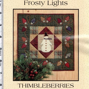 May include: A quilting pattern for a holiday quilt featuring a snowman with a red hat and scarf, surrounded by a string of lights. The pattern is titled "Frosty Lights" and is by Thimbleberries, Classic Country, by Lynette Jensen.