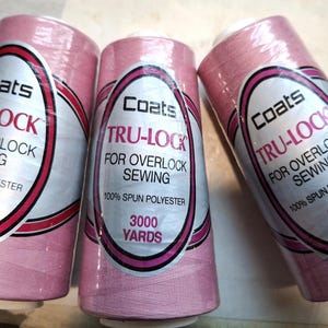 Puede incluir: Tres bobinas rosas de hilo Coats Tru-Lock para coser con overlock. Cada bobina lleva la inscripción "Coats Tru-Lock For Overlock Sewing" y contiene 2743 metros de hilo 100% poliéster hilado.