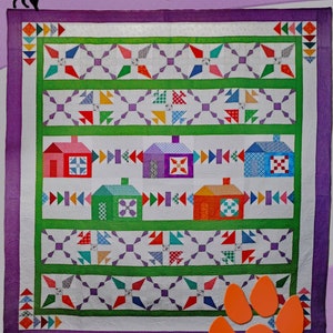 May include: A quilt pattern featuring a community of colorful houses with a green border and purple background. The quilt is 90 inches by 96 inches and includes a bonus table runner. "DEB'S CATS N QUILTS Presents: Community" is written at the top of the image.
