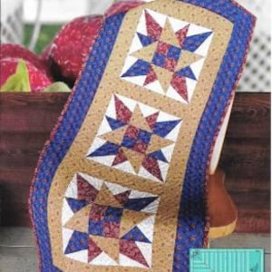 Könnte beinhalten: Ein Quiltmuster für einen Tischläufer namens "Propensity Runner" von Deb's Cats N Quilts Designs. Der Läufer zeigt ein blaues, rotes und braunes Sternmuster. Das Muster enthält Anweisungen für die Verwendung des Creative Grids Kitty Cornered Tool CGRDHS.