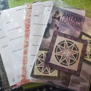 Könnte beinhalten: Ein Quiltmusterheft mit einem Leuchtturm auf dem Cover. Der Titel lautet "Antique Lighthouse" und der Untertitel "Timeless Treasures". Das Heft enthält Anleitungen zum Nähen eines Quilts mit einem sternförmigen Design.