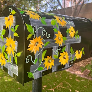 May include: Black mailbox with a hand-painted design of sunflowers and vines. The mailbox is decorated with a white trellis pattern and green leaves.