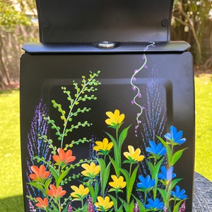 May include: Black metal mailbox with a hand-painted floral design. The design features yellow, orange, blue, and purple flowers on a black background.