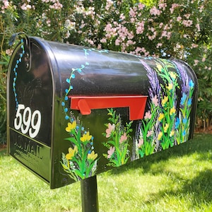 May include: Black mailbox with a floral design painted on the front. The mailbox has a red flag and the number 599 is painted on the side.