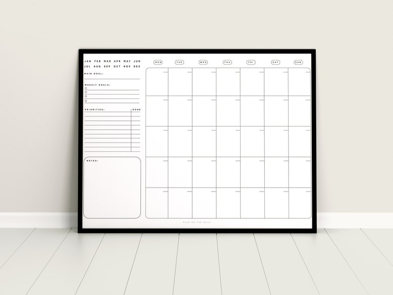 May include: A black and white monthly calendar planner with a black frame. The calendar has sections for weekly goals, priorities, and notes. The calendar is labeled with the months of the year and days of the week.