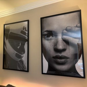 May include: Two framed black and white art prints hanging on a beige wall. One print features a racing helmet, and the other is a close-up portrait of a person's face. Both prints are in black frames.