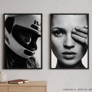 May include: Black and white framed art print set. One print features a person wearing a motorcycle helmet. The other print is a close-up of a person's face with a hand covering one eye. The set is displayed on a wooden surface.