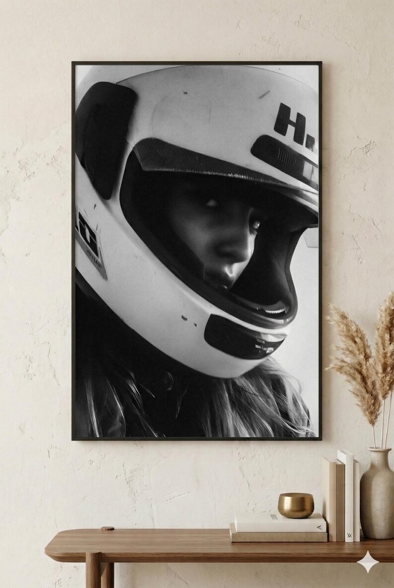 May include: Black and white framed print of a person wearing a white motorcycle helmet. The helmet has a dark visor and the letter "H" on the side. The person's face is partially visible, with long hair flowing out from under the helmet.