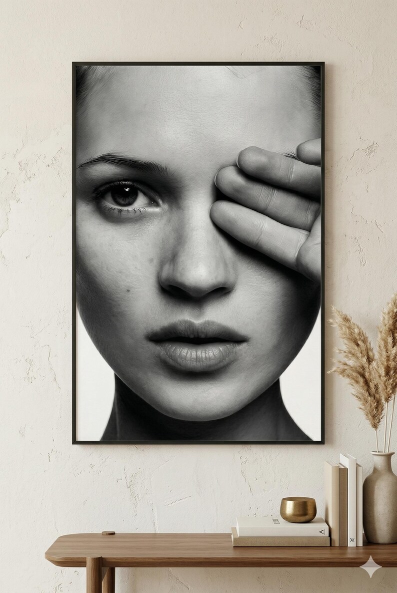 May include: Black and white framed portrait of a person with their hand covering one eye. The image is a close-up, focusing on the face and hand. The person's skin is smooth, and the image has a high contrast.