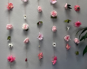 May include: A wall decoration with multiple strands of pink flowers and leaves hanging from a wooden dowel.