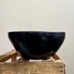 May include: A black ceramic bowl with a rounded shape. The bowl is sitting on a wooden crate.