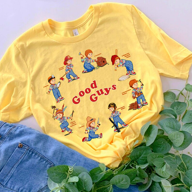 May include: Yellow t-shirt with a graphic of various characters from the movie Child's Play. The characters are all depicted as "good guys" and have different professions. The text "Good Guys" is printed in red on the shirt.