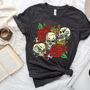 May include: A dark grey t-shirt with a graphic print of three white skulls surrounded by red, yellow, and white flowers.