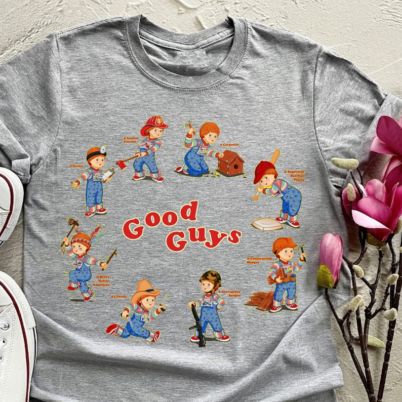 May include: Gray t-shirt with a graphic print of eight cartoon characters in different outfits and poses. The characters are all holding tools or playing sports. The text "Good Guys" is printed in large letters below the characters.