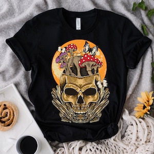 May include: Black t-shirt with a graphic of a skull with mushrooms growing out of the top. The skull is surrounded by a yellow and orange sun. There are butterflies and leaves around the skull.
