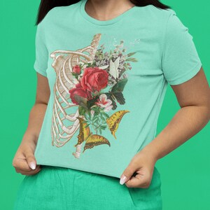 May include: A light blue t-shirt with a floral and skeletal design. The design features a ribcage with flowers, butterflies, and leaves.