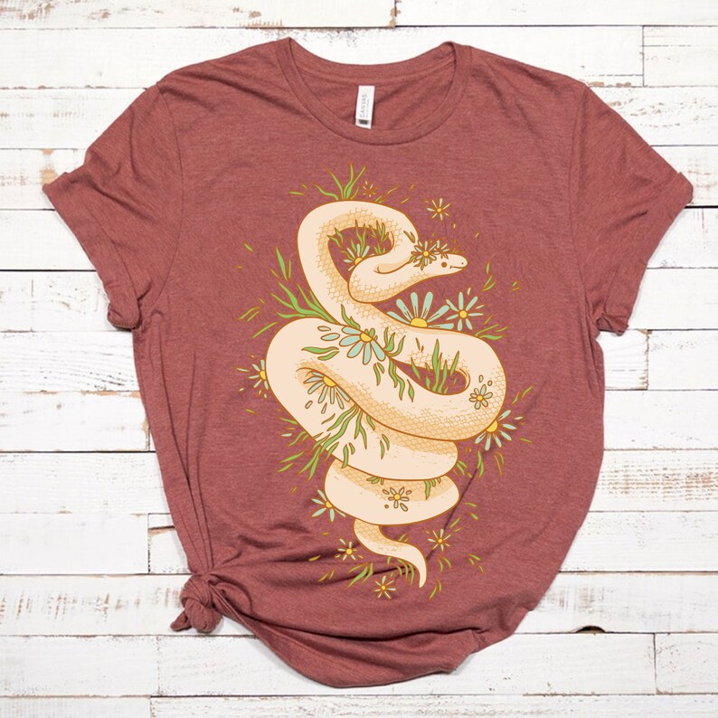 May include: A maroon t-shirt with a white snake design. The snake is curled up in a circle and surrounded by green leaves and white flowers.